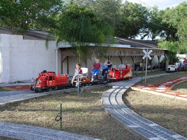 Children riding a red miniature train past the station building