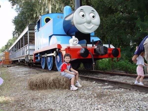 Child posing next to a blue tank engine miniature locomotive