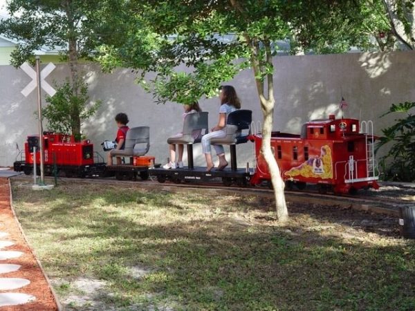 Children riding a red miniature train under the trees